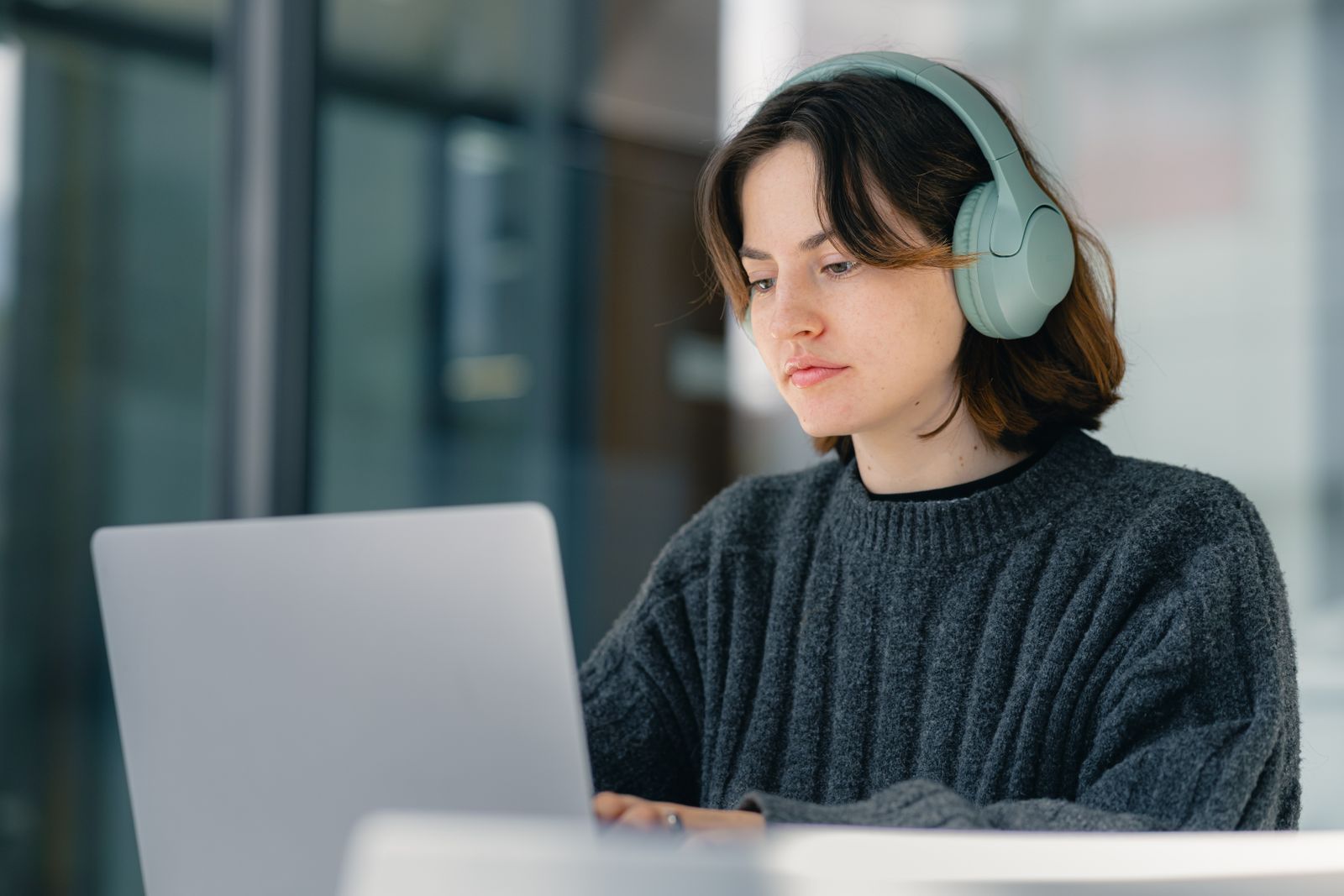 A reviewer wearing headphones works through audio at her laptop